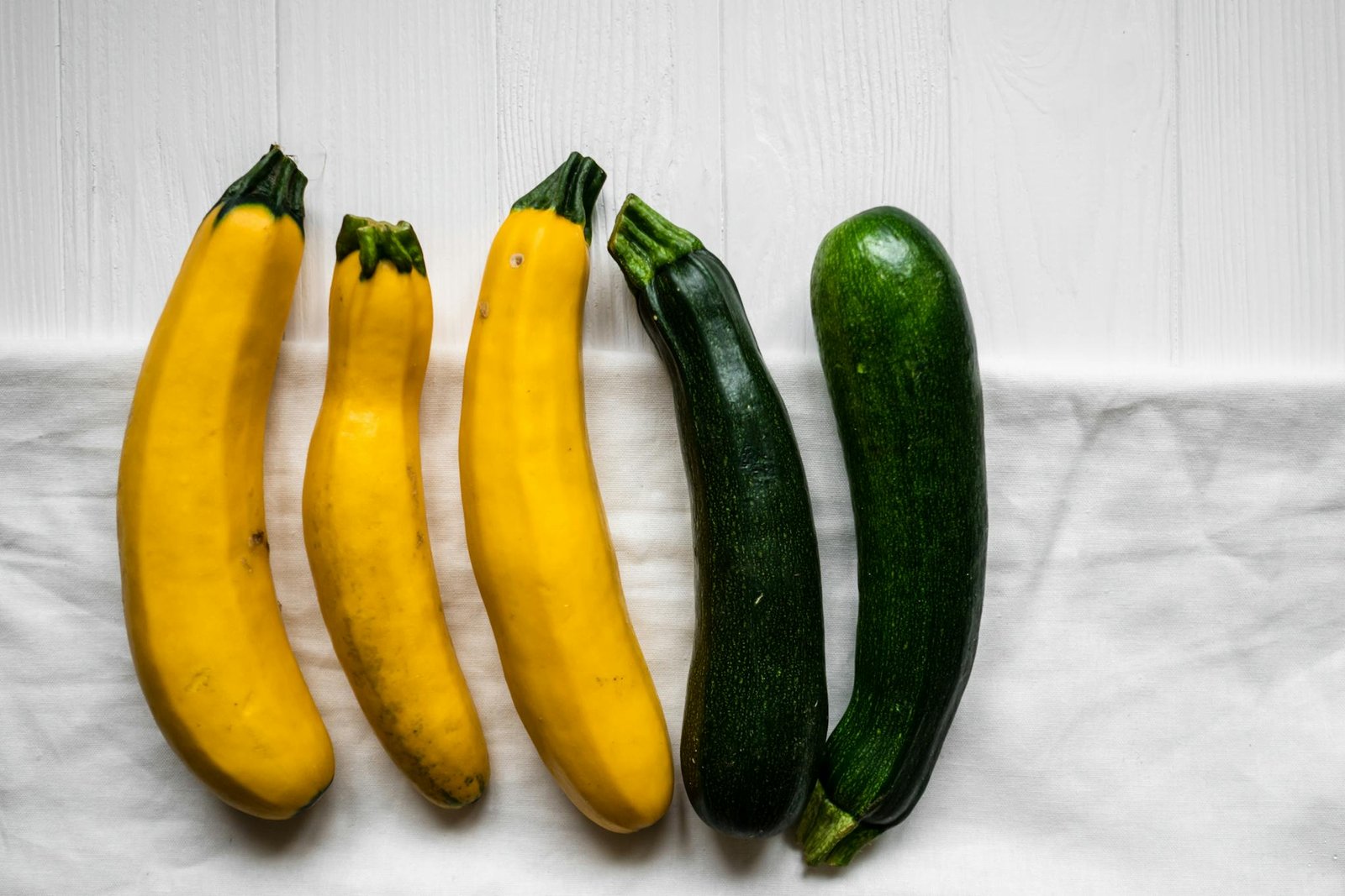 A variety of fresh zucchini and yellow squash on a white cloth background, ideal for healthy cooking.