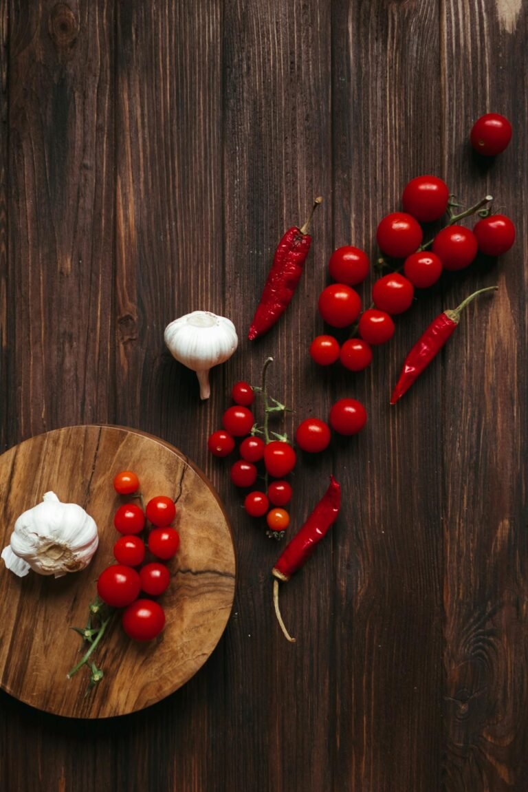 Overhead view of cherry tomatoes, garlic, and chili peppers on a wooden surface.